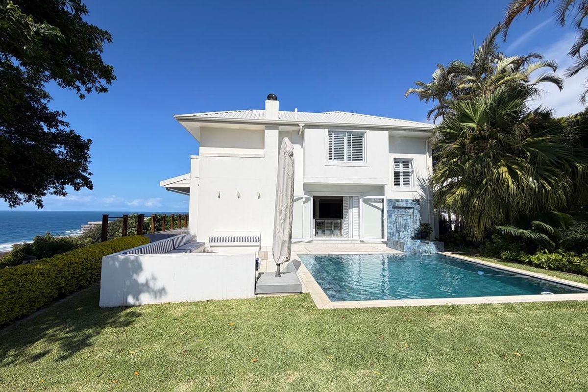 Rear exterior view featuring a swimming pool, built-in seating area, and landscaped garden with ocean views.