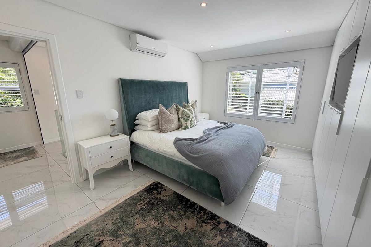 A modern, well-maintained bedroom featuring polished tiled floors, built-in wardrobes, split-system air conditioning, and louvre shutters for natural light control.