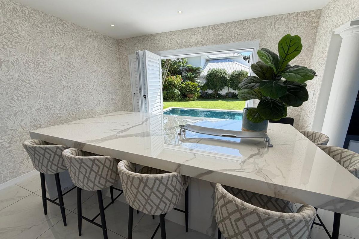 Modern kitchen featuring a large stone waterfall island, patterned wallpaper, and bi-fold doors opening directly to the pool area.