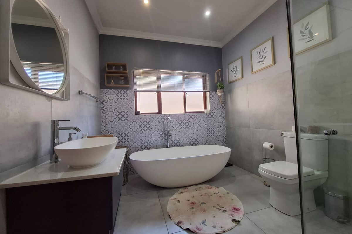 Modern bathroom featuring a freestanding bathtub, a vessel sink vanity, a glass-enclosed shower, and decorative patterned wall tiling.