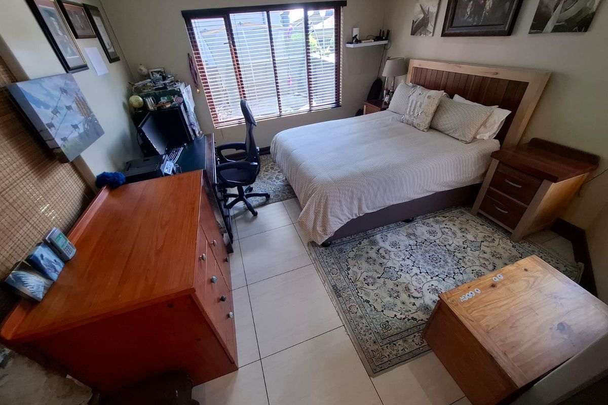 A functional bedroom featuring tiled flooring, a large window with fitted blinds, and neutral wall finishes.