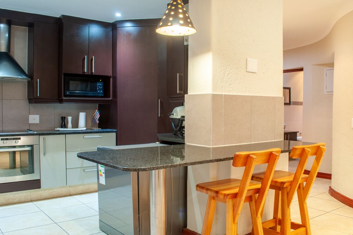 Modern kitchen featuring dark wood cabinetry, granite countertops, a built-in oven, stainless steel extractor fan, and a breakfast bar with tiled flooring.