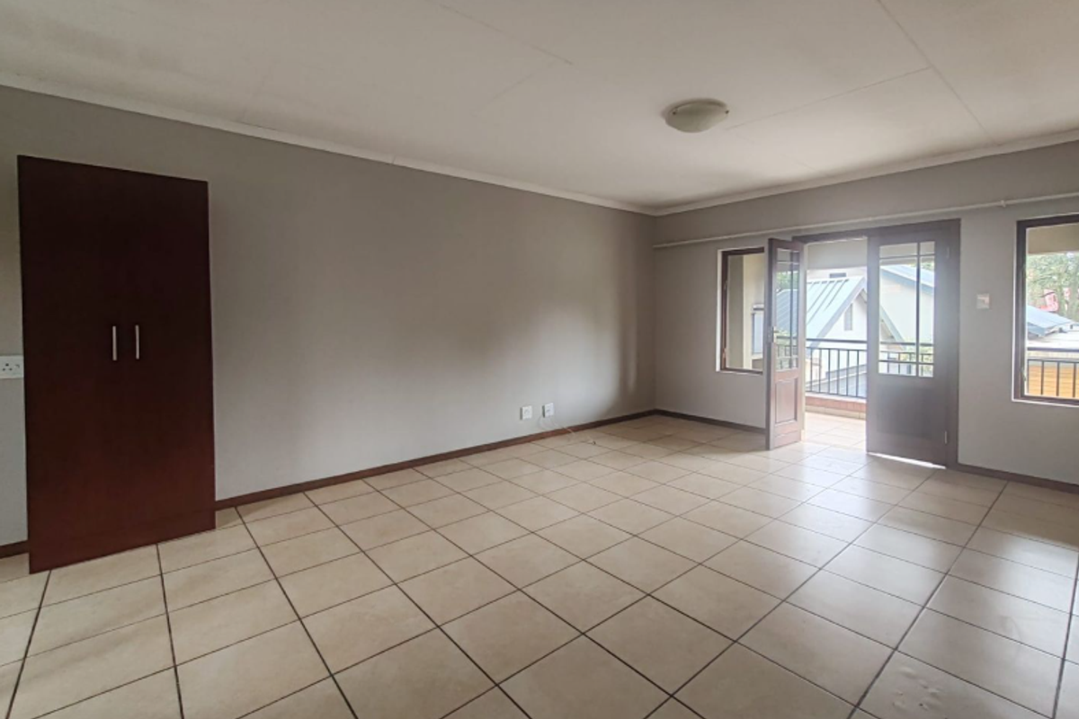 Spacious living area featuring neutral tiled flooring, a built-in cupboard, and direct access to a private balcony through glass-paneled doors.