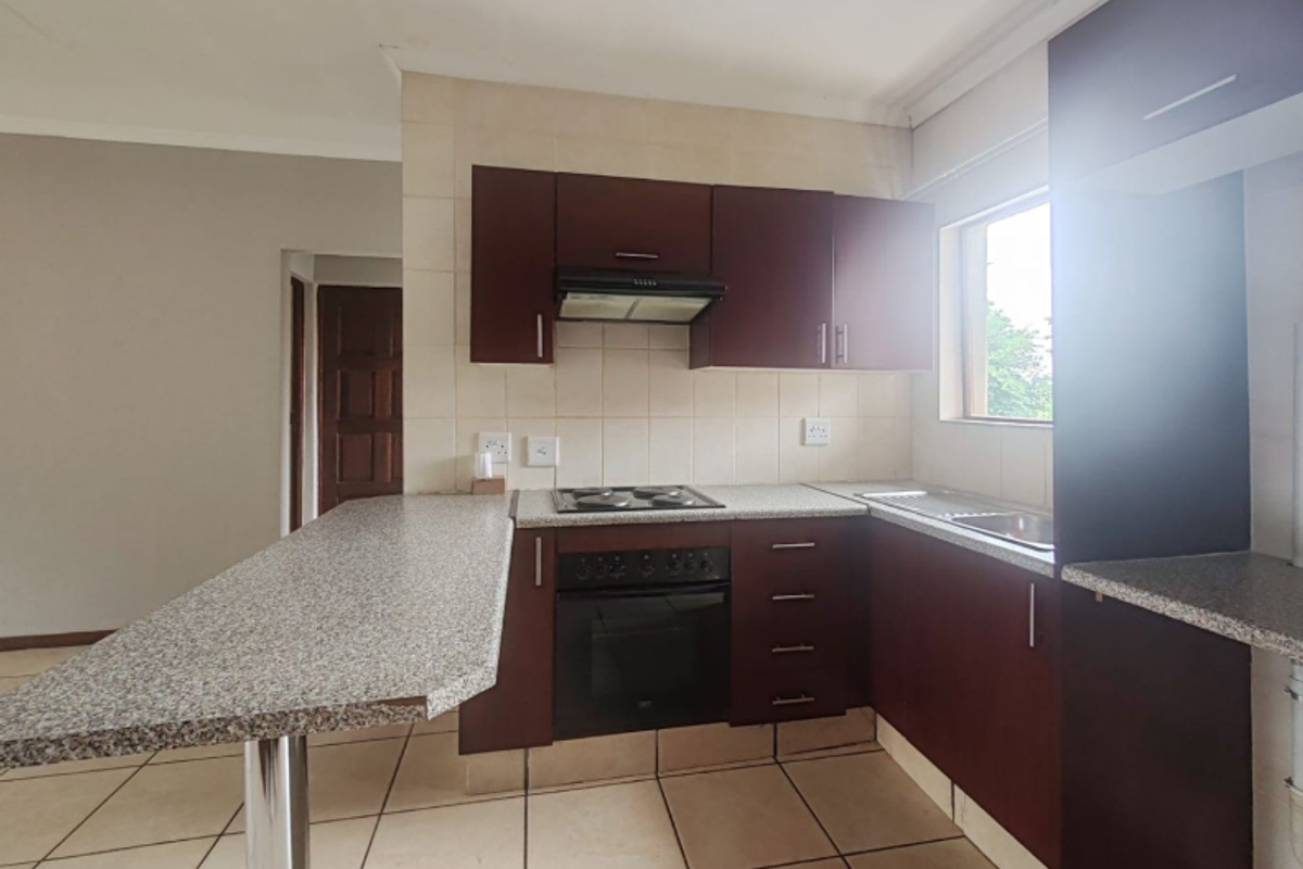 A functional kitchen featuring dark wood cabinetry, granite-look countertops, a built-in oven, hob, extractor fan, and a breakfast bar extension.