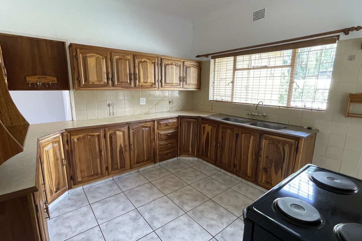 A functional kitchen featuring traditional wooden cabinetry, tiled countertops, a double basin sink, and tiled flooring with a large window for natural light.