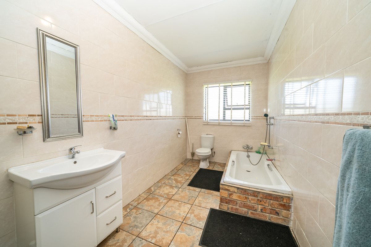 A functional bathroom featuring a vanity basin, a built-in bathtub with brick surround, and full-height wall tiling.