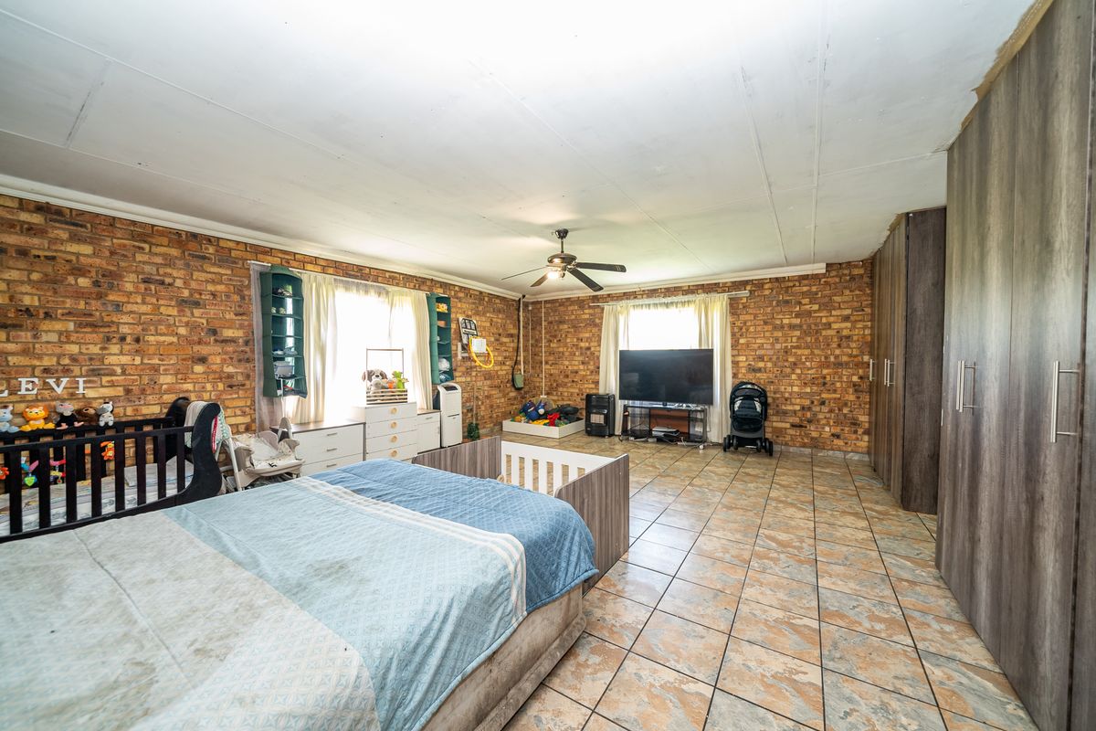 Spacious bedroom featuring exposed brick walls, tiled flooring, and built-in wooden cupboards, offering a rustic aesthetic with ample storage space.