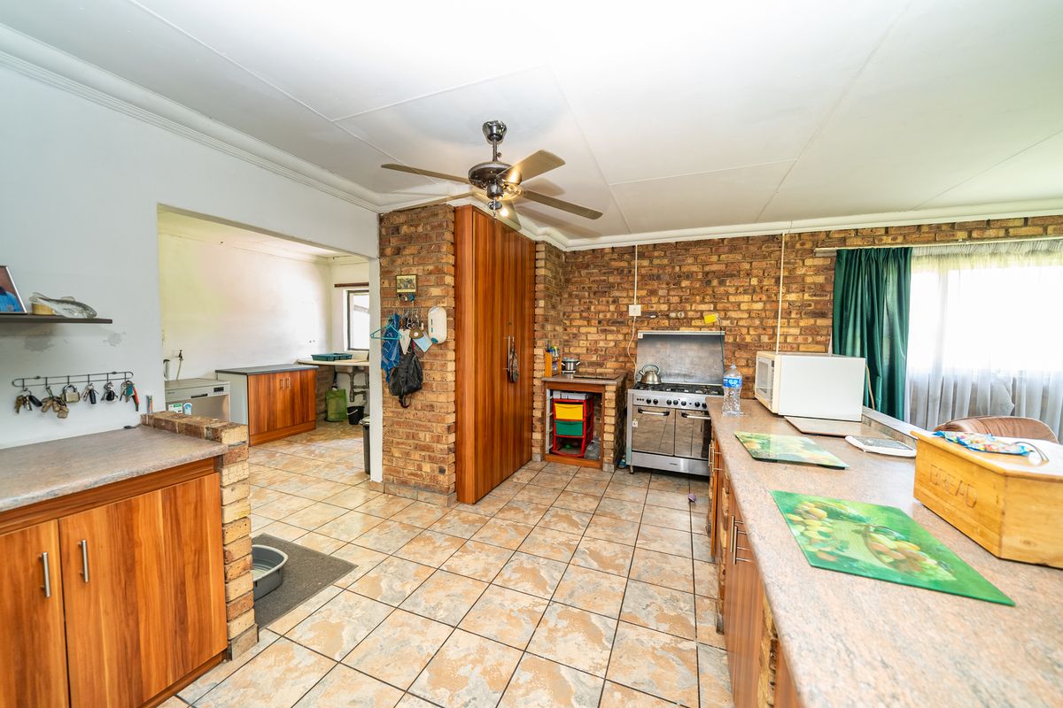 Rustic farm-style kitchen featuring exposed brick walls, wooden cabinetry, tiled flooring, and a functional gas stove, with an adjoining scullery area.
