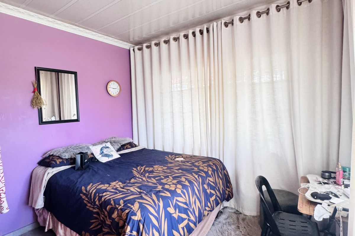 A bedroom featuring tiled flooring, a purple accent wall, and a large window covered by floor-to-ceiling curtains.