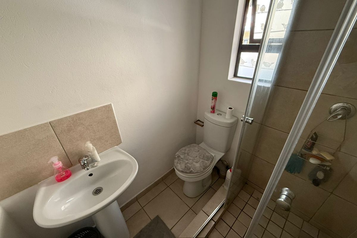 A functional bathroom featuring a pedestal basin, toilet, and a glass-enclosed shower with neutral floor and wall tiling.