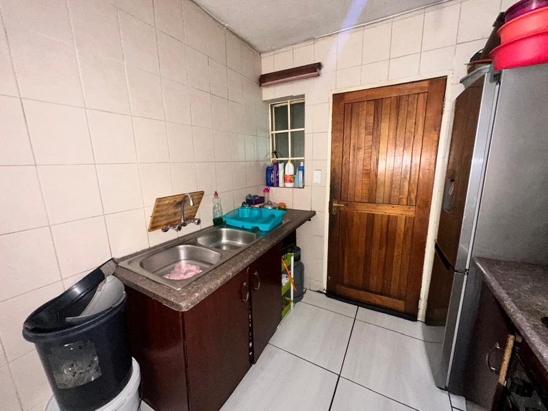 A functional scullery area featuring a double stainless steel sink, laminate countertops, built-in cabinetry, and tiled finishes throughout.