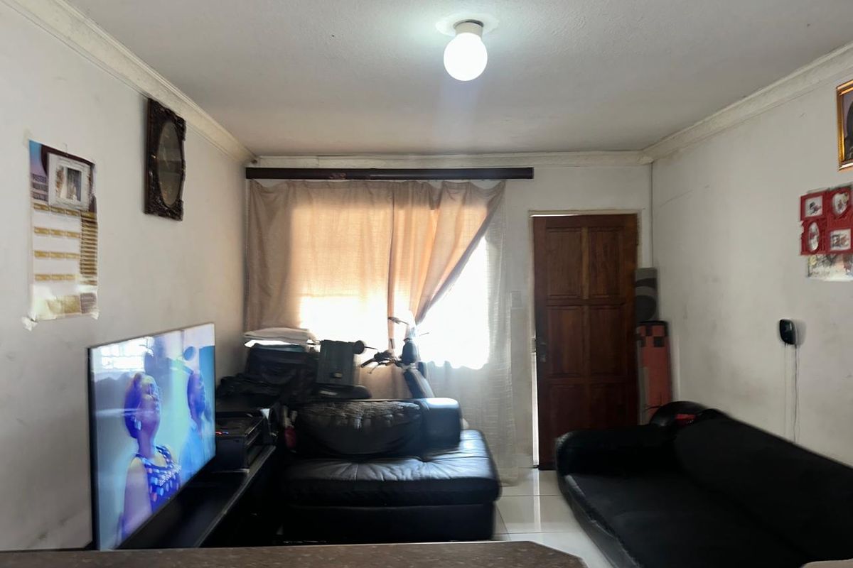 A living room area featuring tiled flooring, a wooden door, and coving, currently showing signs of wear on the walls and ceiling.