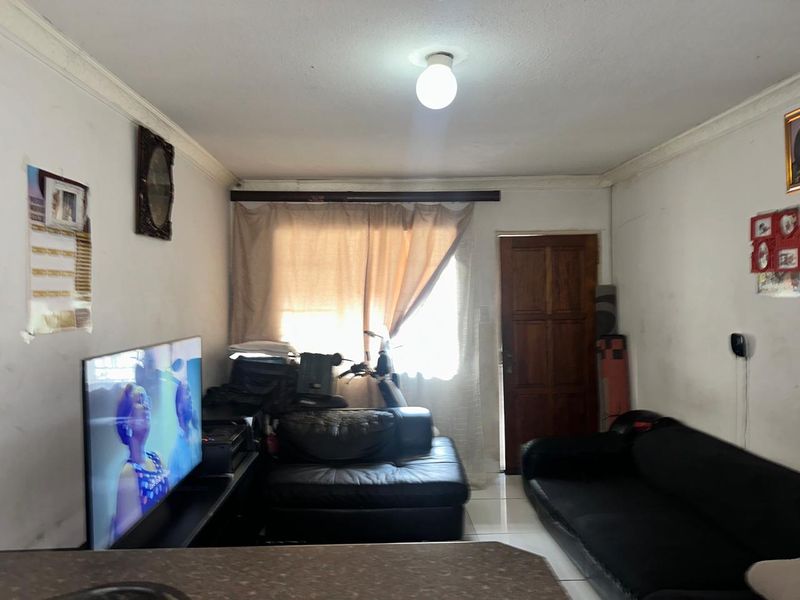 A living room area featuring tiled flooring, a wooden door, and coving, currently showing signs of wear on the walls and ceiling.