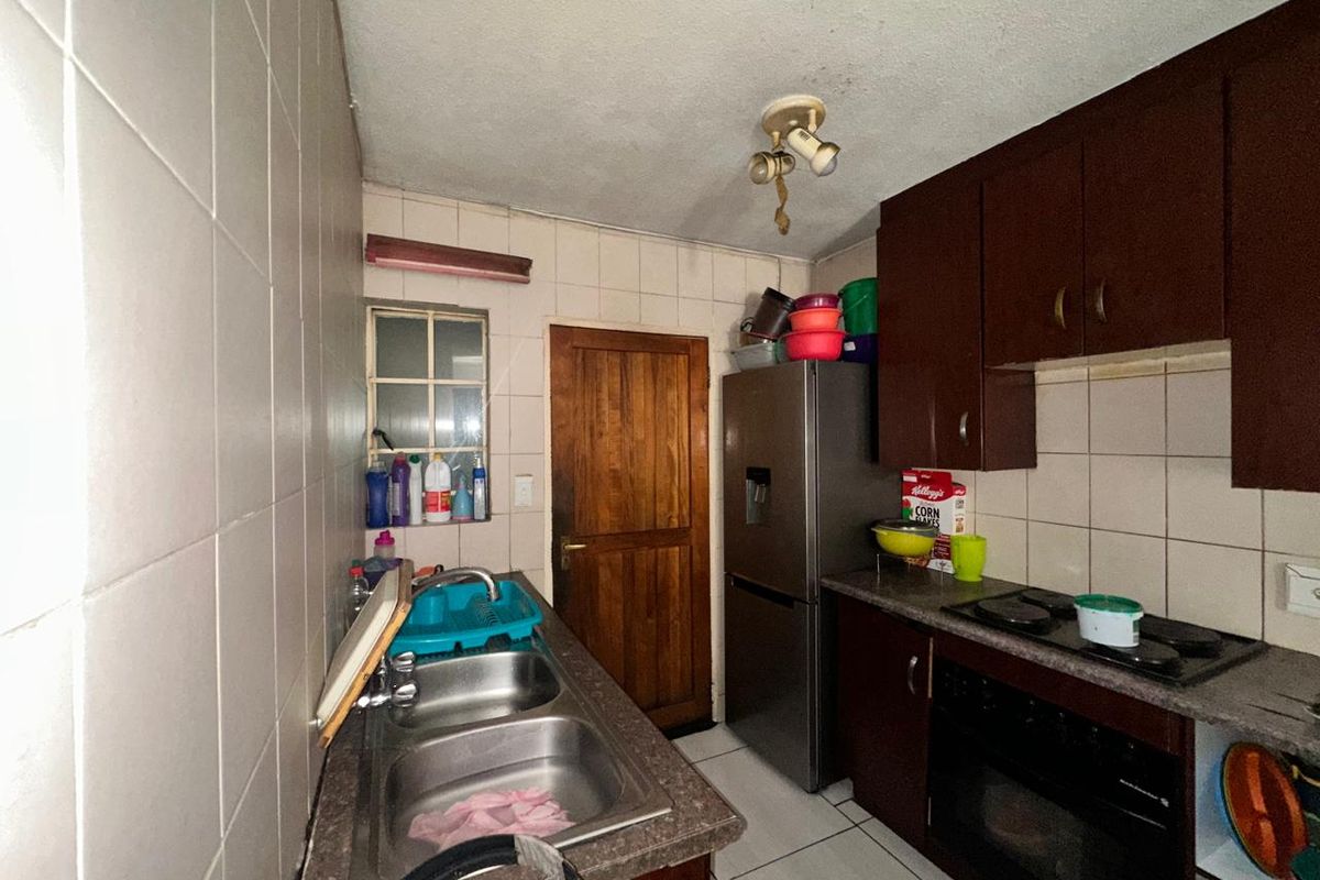 Compact kitchen featuring dark cabinetry, built-in oven and hob, double stainless steel sink, and tiled splashbacks.