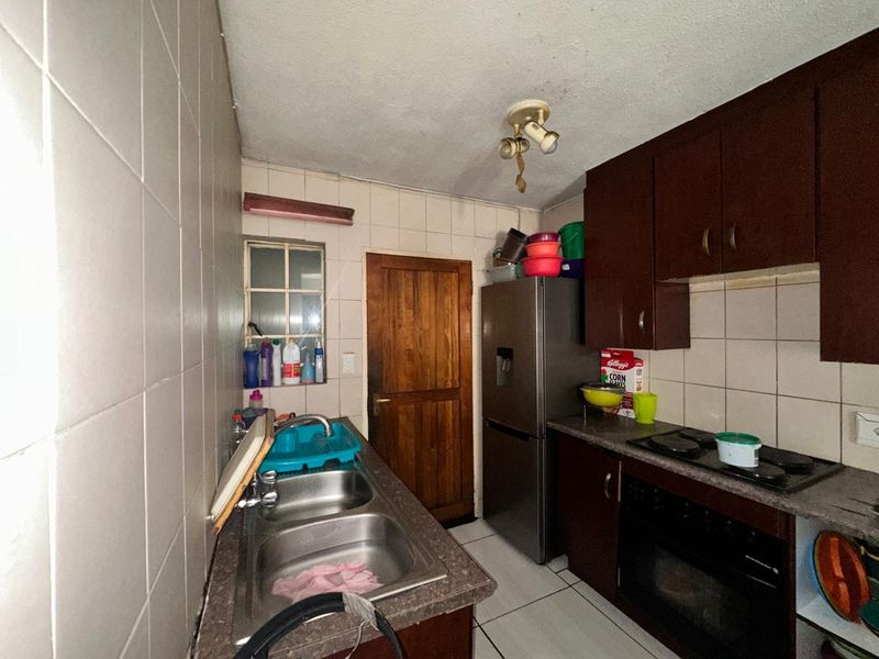 Compact kitchen featuring dark cabinetry, built-in oven and hob, double stainless steel sink, and tiled splashbacks.