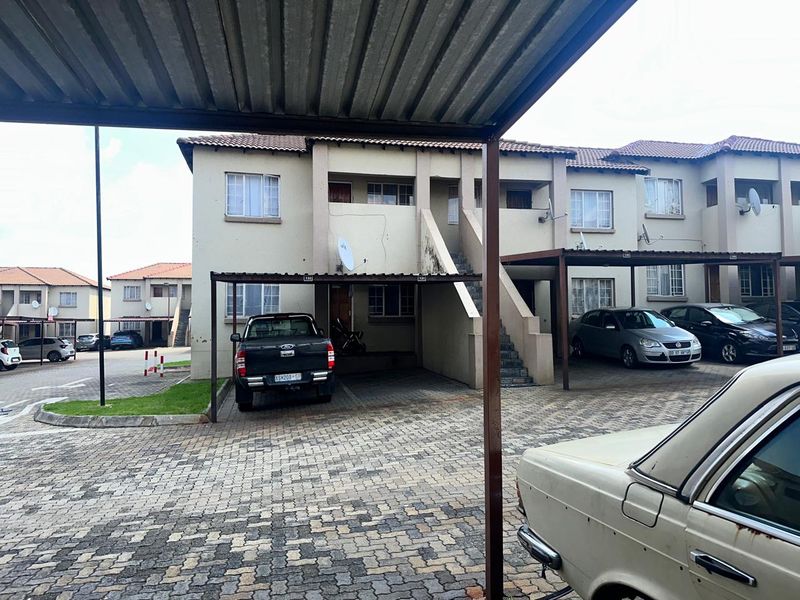 Exterior view of a multi-story flat complex featuring paved parking areas, covered carports, and external staircases.
