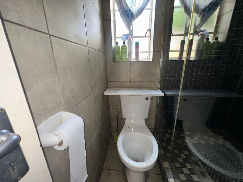 Compact bathroom featuring a toilet, shower enclosure, and neutral wall tiling. The space requires minor maintenance to address tile and grout wear.