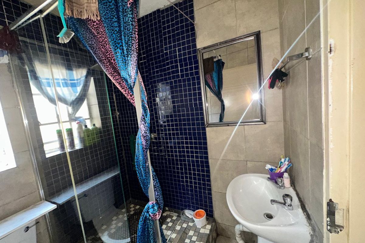 A dated bathroom featuring a pedestal basin, shower enclosure, and blue mosaic wall tiling, requiring significant renovation and finish repairs.