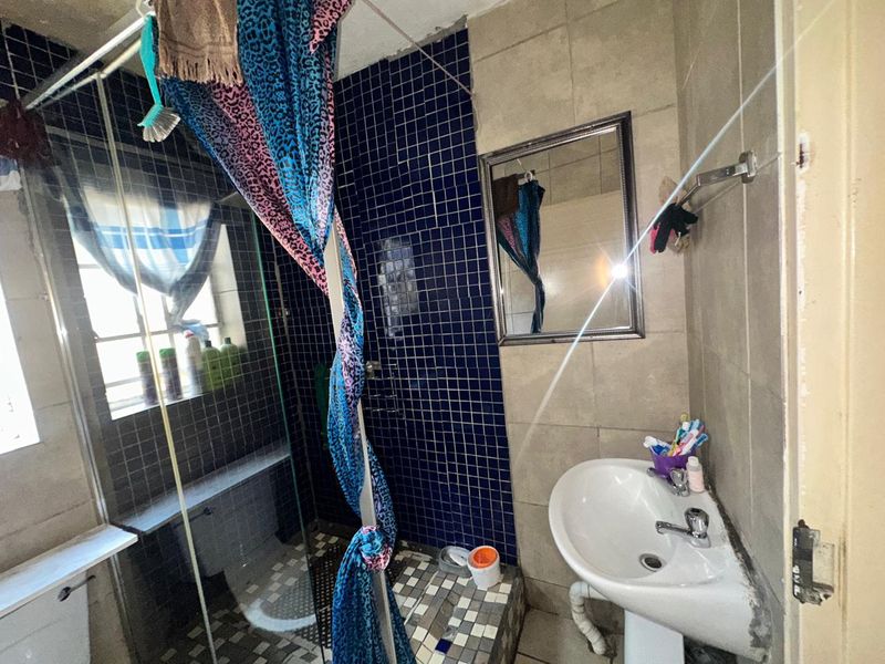 A dated bathroom featuring a pedestal basin, shower enclosure, and blue mosaic wall tiling, requiring significant renovation and finish repairs.