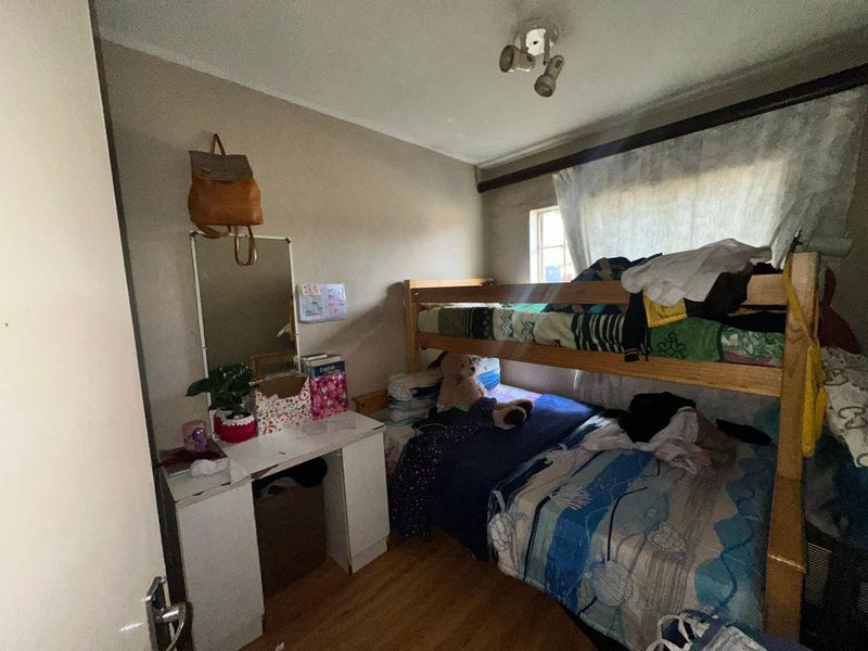 A compact bedroom featuring laminate flooring and a ceiling-mounted spotlight fixture, offering a functional space that could benefit from cosmetic updates.