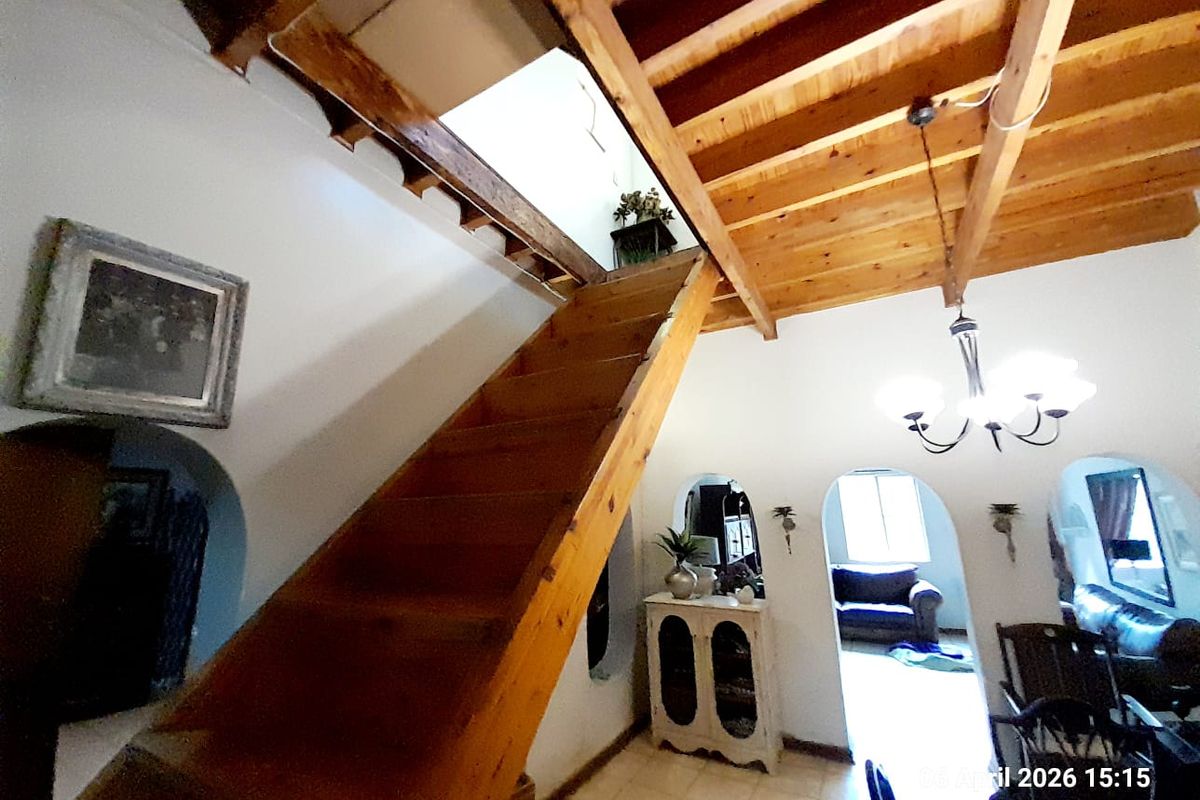 Interior view featuring a rustic wooden staircase leading to an upper level, exposed timber beam ceiling, and arched doorways connecting to adjacent living spaces.