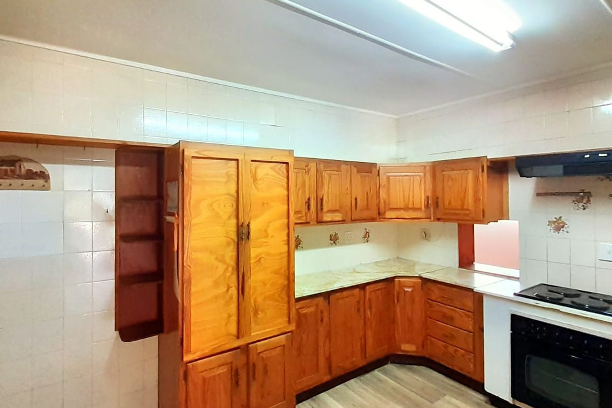 A functional kitchen featuring traditional wooden cabinetry, tiled splashbacks, and a built-in oven with extractor fan, offering a classic layout ready for modernization.
