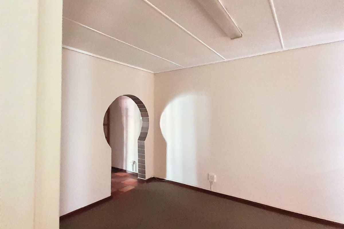 An empty living area featuring a distinctive arched doorway, neutral walls, and carpeted flooring, offering a blank canvas for potential renovation.