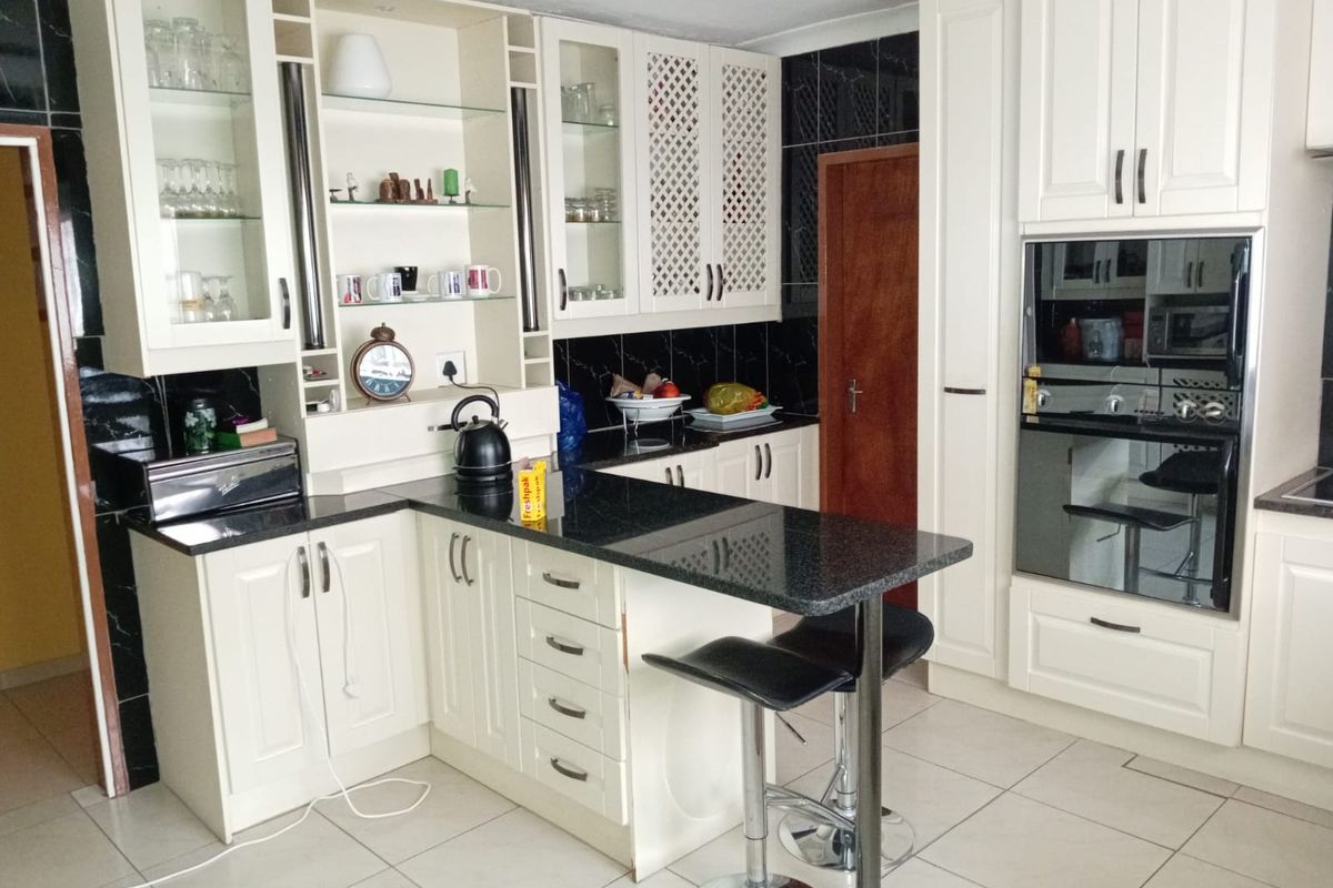 A functional kitchen featuring white cabinetry, black granite countertops, a breakfast bar, and built-in oven and microwave units.