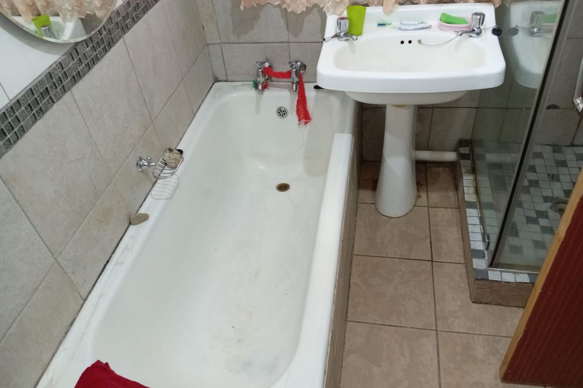 A compact bathroom featuring a standard bathtub, pedestal basin, and a glass-enclosed shower with tiled walls and flooring.