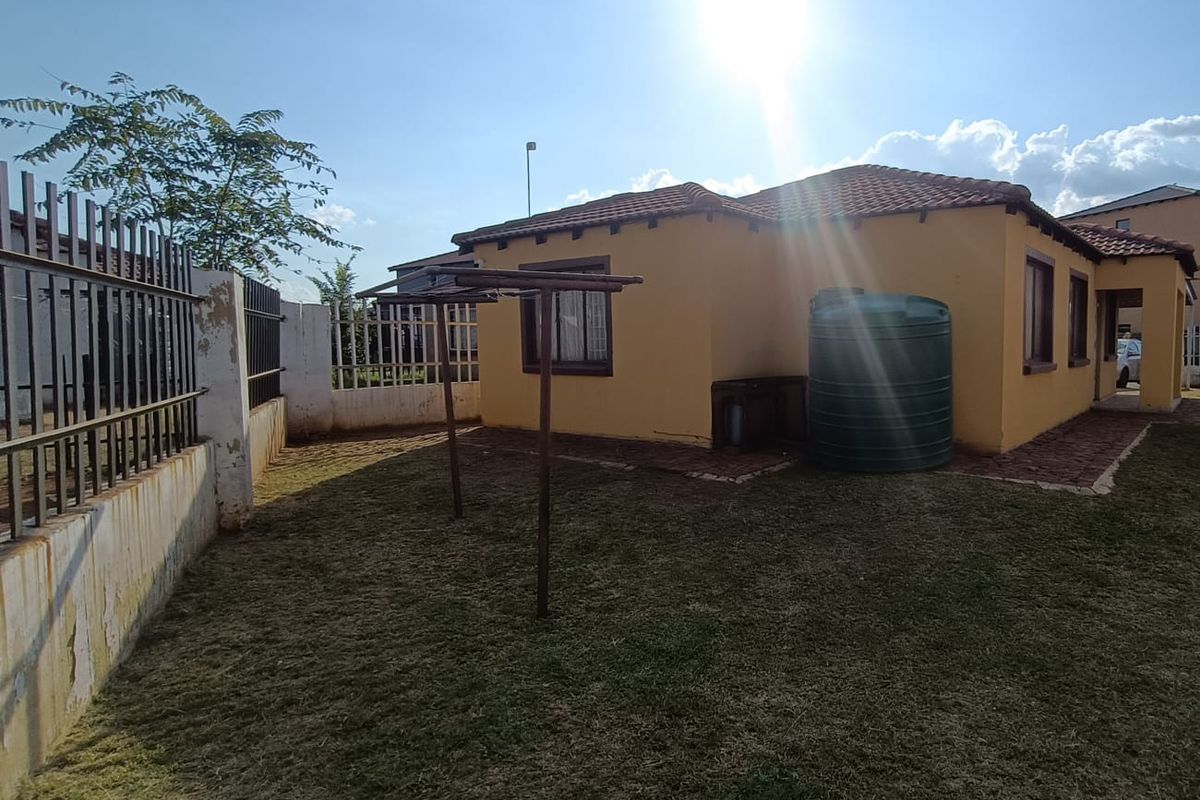 Rear exterior view of the house featuring a garden area, paved walkway, and a large water storage tank.