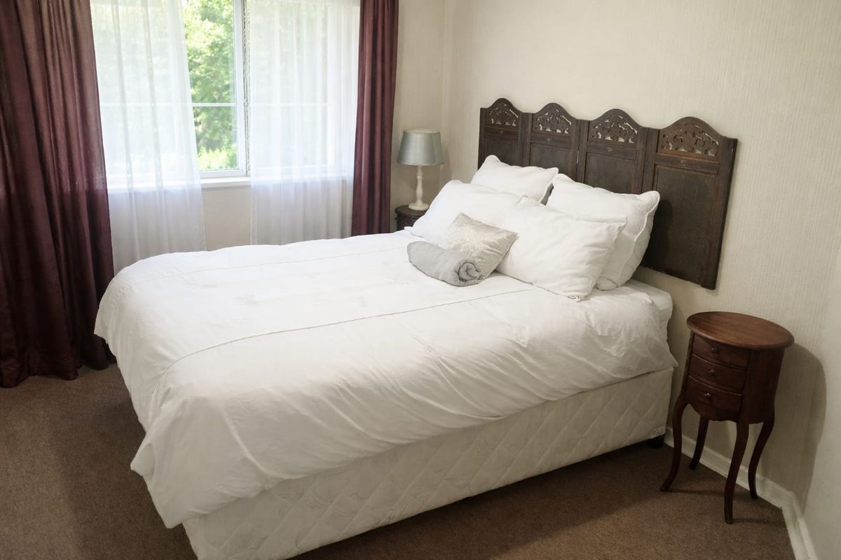 A well-lit bedroom featuring neutral wall finishes, carpeted flooring, and a large window providing natural light.