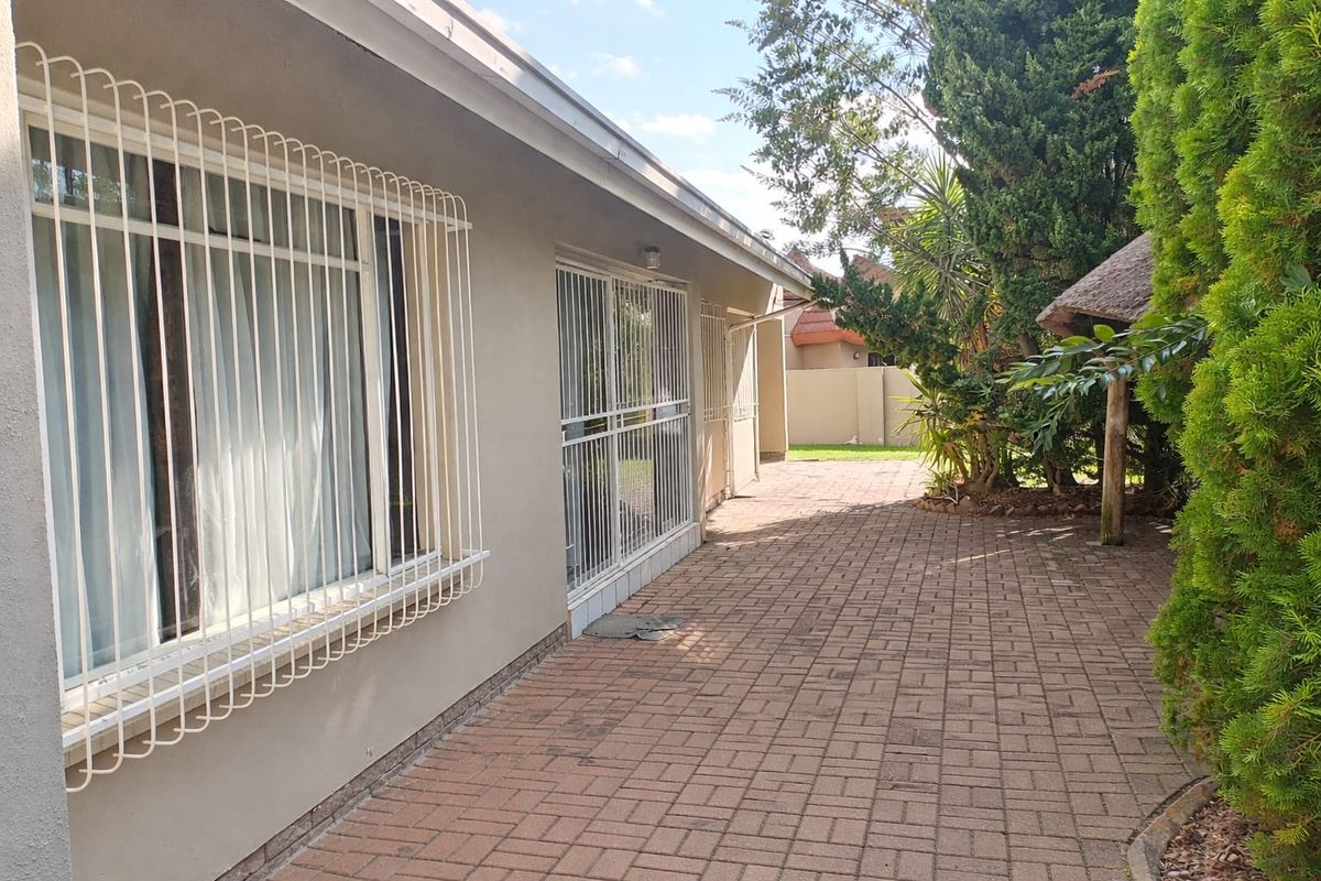 A paved rear patio area featuring security bars on windows and doors, adjacent to a landscaped garden with mature trees.