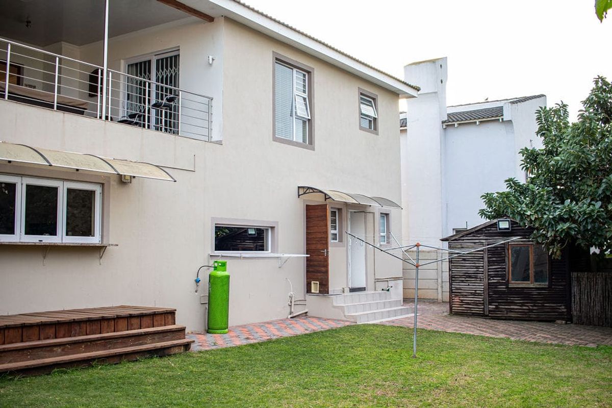 Rear exterior view of the property featuring a paved patio area, small lawn, wooden garden shed, and an elevated balcony with stainless steel railings.