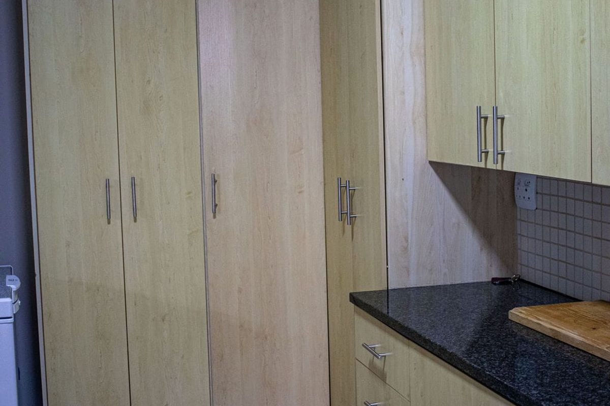 A functional kitchen area featuring light wood-finish cabinetry, dark granite countertops, and tiled flooring.