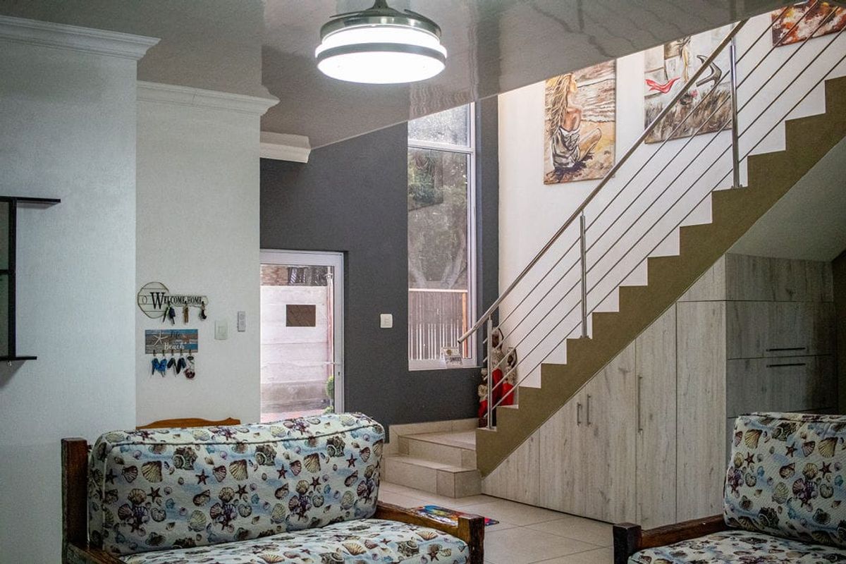 A bright living area featuring a staircase with integrated under-stair storage cabinetry, modern stainless steel railings, and high ceilings with recessed lighting.