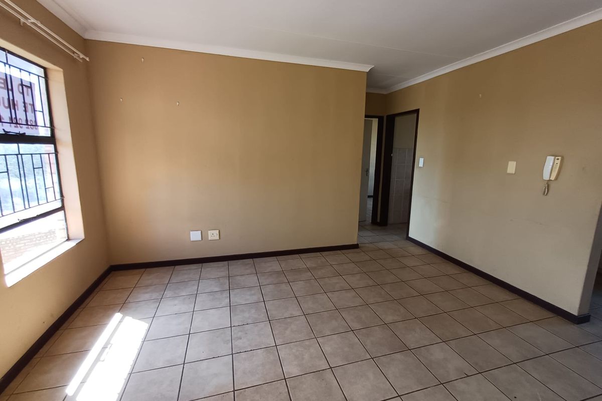 An empty living room featuring neutral tiled flooring, beige walls, and a window with security bars.