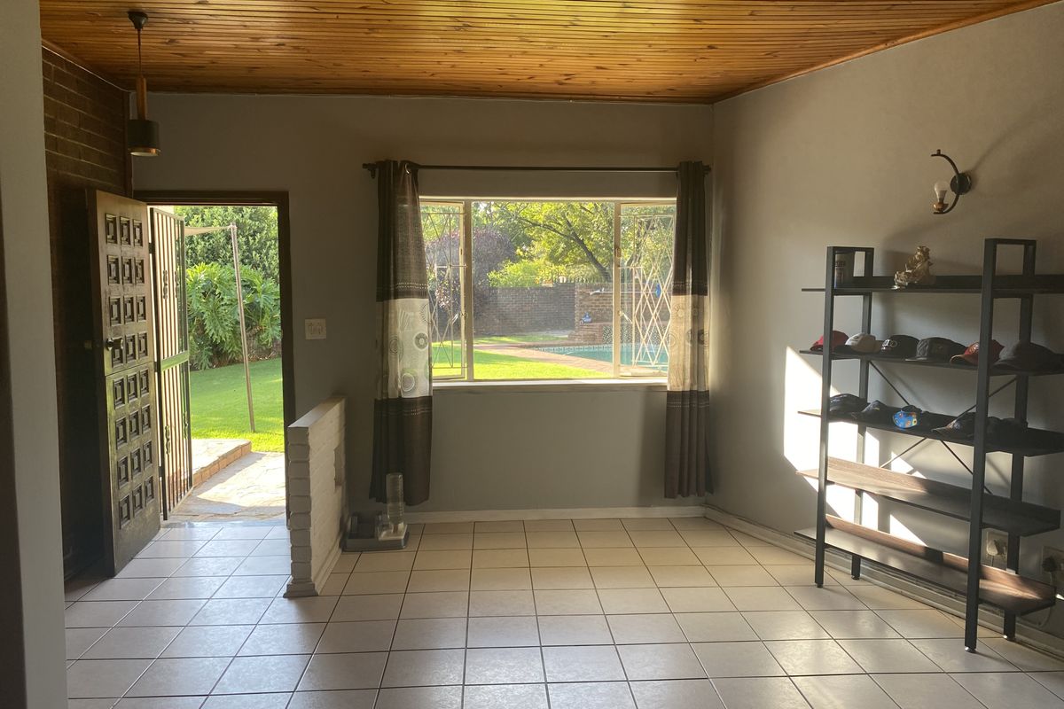 A living area featuring tiled flooring, a timber-paneled ceiling, and direct access to an outdoor garden and pool area through a side entrance.