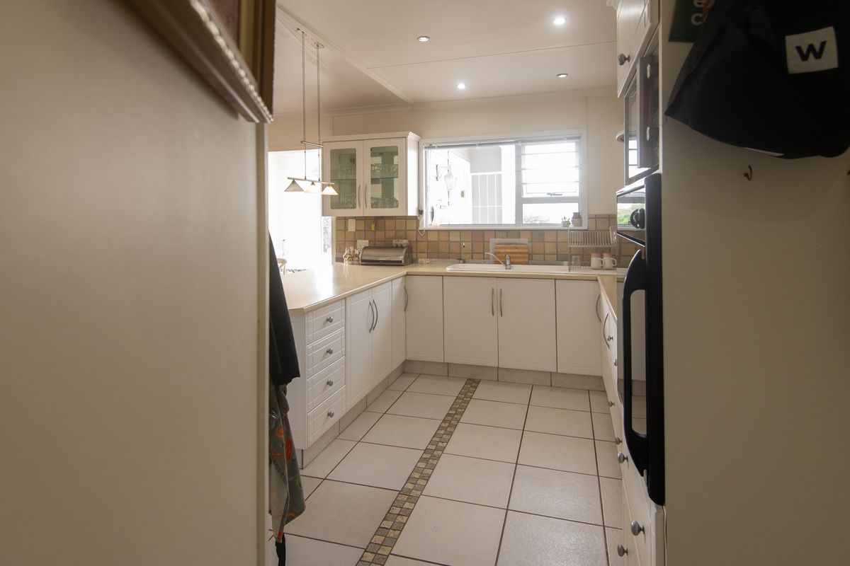 A functional kitchen featuring white cabinetry, tiled splashbacks, built-in oven, and tiled flooring with a decorative inlay.