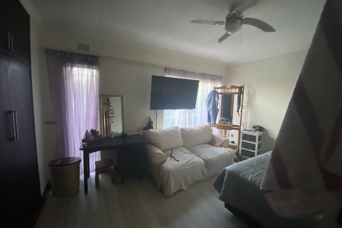 A bedroom featuring built-in cupboards, a ceiling fan, and light-toned flooring, offering a functional living space.