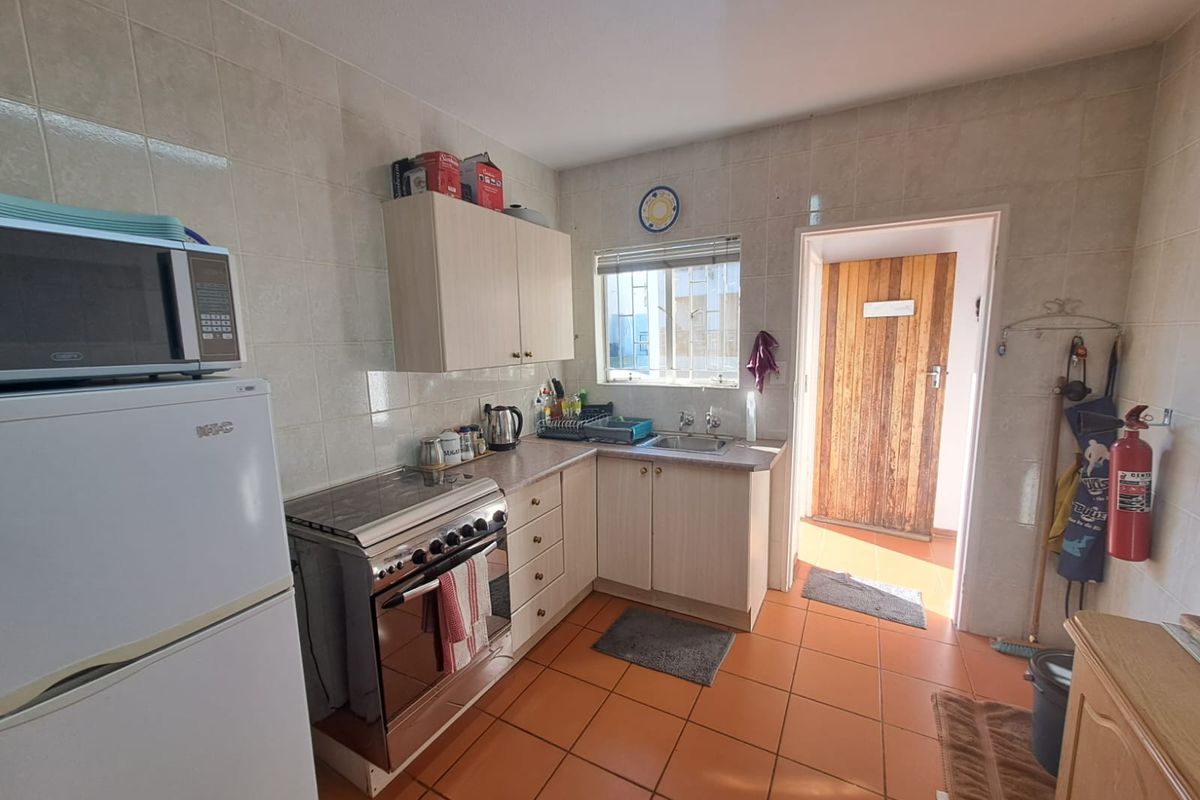 A functional kitchen featuring tiled walls, laminate countertops, built-in cabinetry, and a freestanding stove, with direct access to an exterior door.