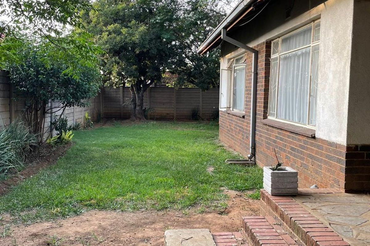 A rear garden view featuring a brick facade, concrete patio steps, and a lawn area enclosed by perimeter walling.