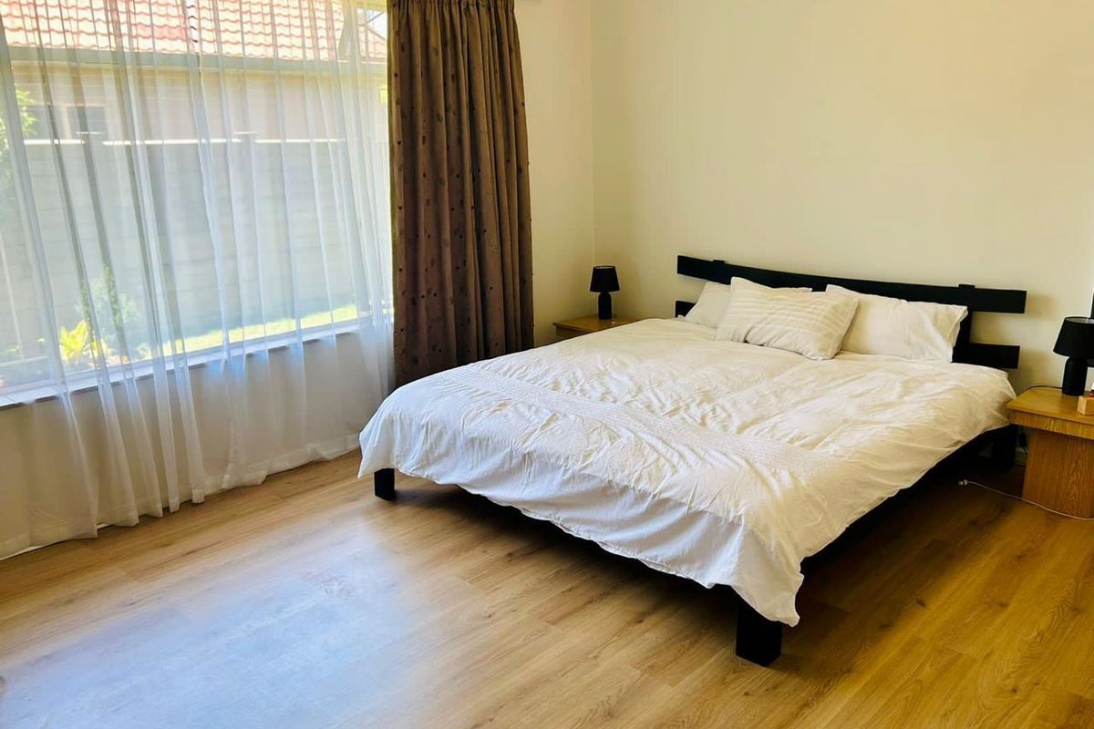 A bright bedroom featuring light wood-look flooring and a large window with curtain treatments.