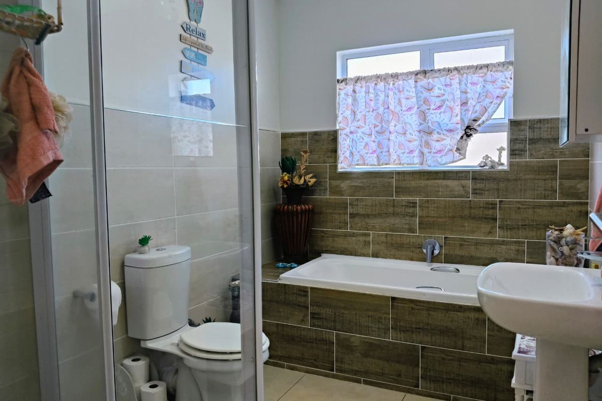 A functional bathroom featuring a built-in bathtub with wood-look tile surround, a separate glass-enclosed shower, a pedestal basin, and a standard toilet.