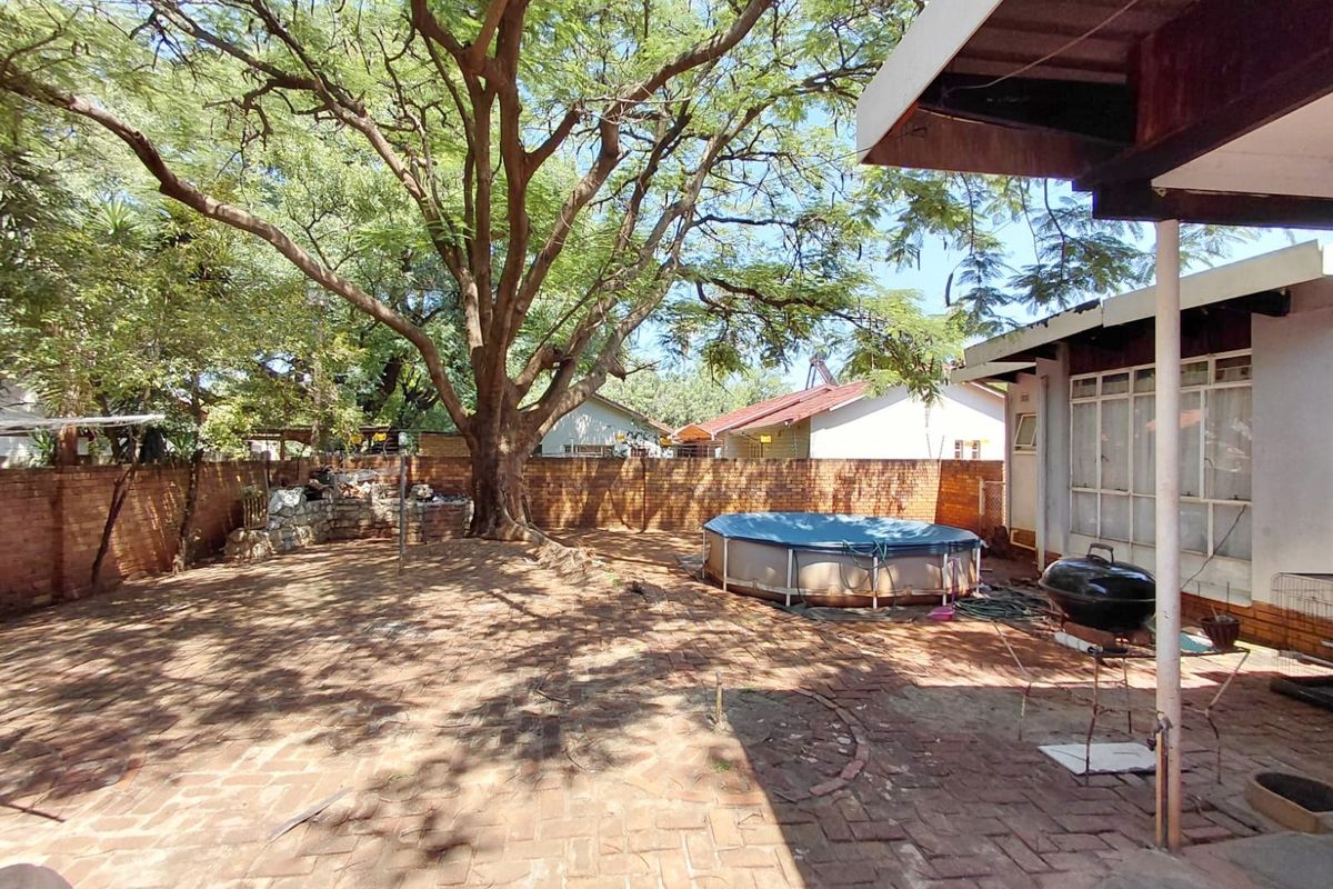 A spacious rear garden featuring extensive brick paving, mature trees, and a covered patio area, providing a private outdoor space.