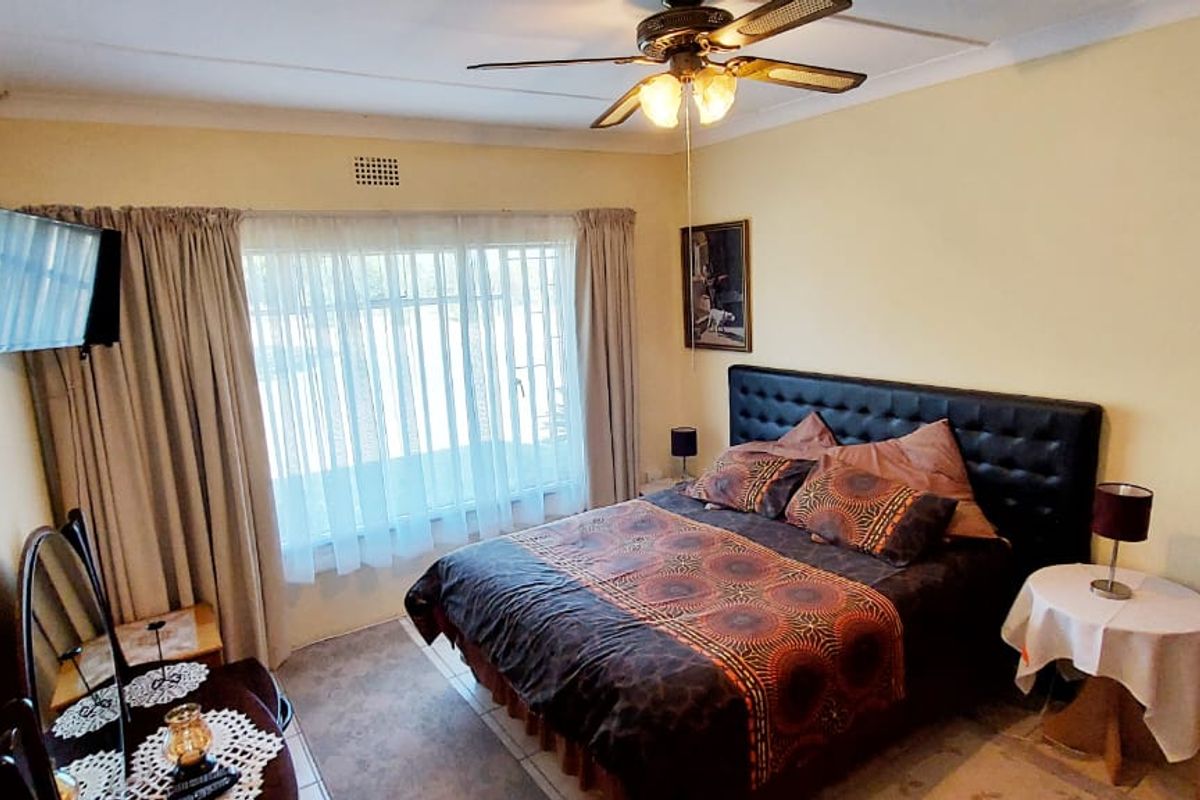A bedroom featuring tiled flooring, a ceiling fan, and a window with security bars, providing a functional and lived-in space.