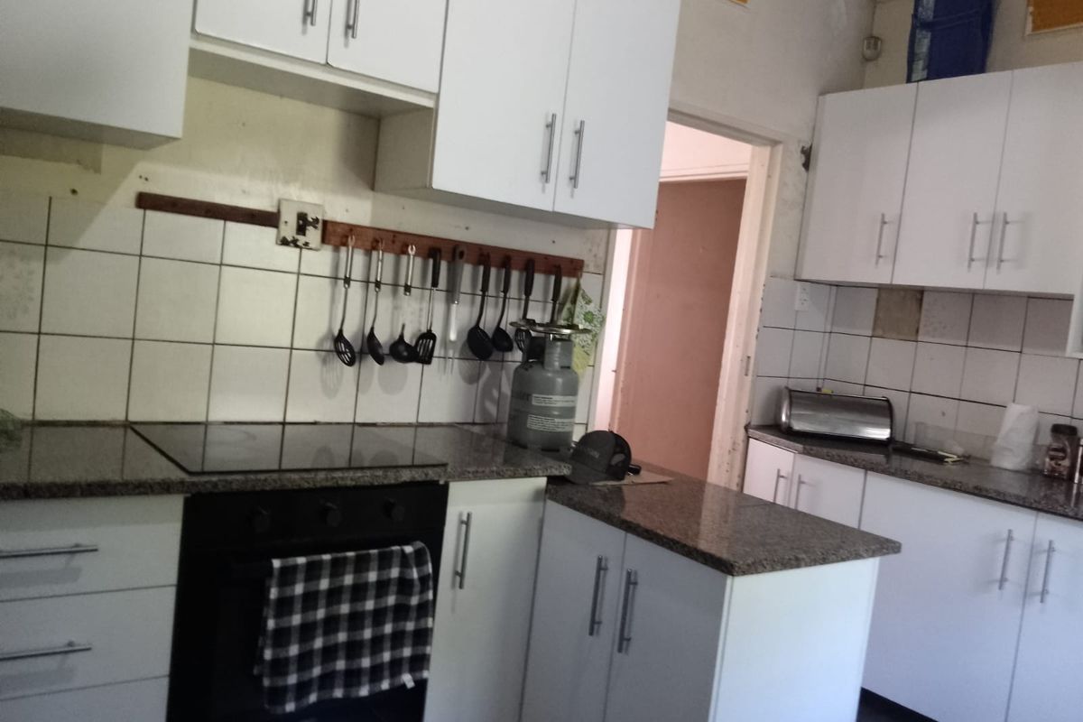 A functional kitchen featuring white cabinetry, granite-look countertops, a built-in oven, and a glass hob with tiled splashbacks.