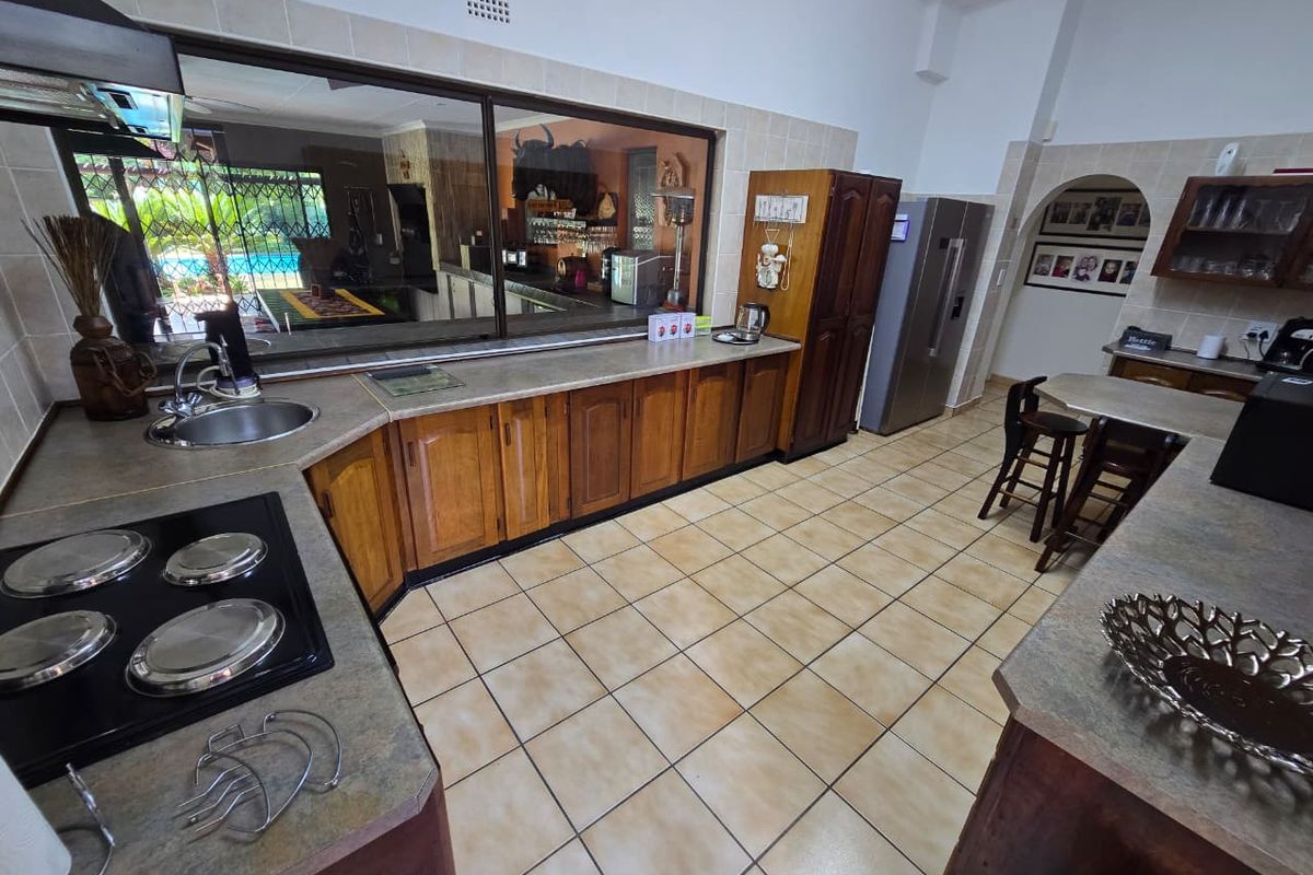 Spacious kitchen featuring wooden cabinetry, integrated hob, double sink, and a large serving window overlooking the outdoor area.