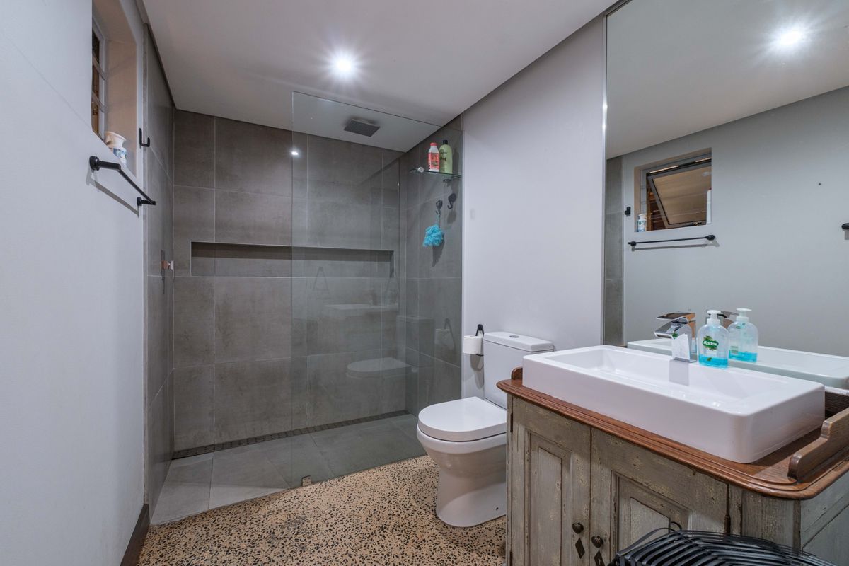 Modern bathroom featuring a walk-in shower with grey tiling, a built-in wall niche, a white ceramic basin, and a vanity unit.
