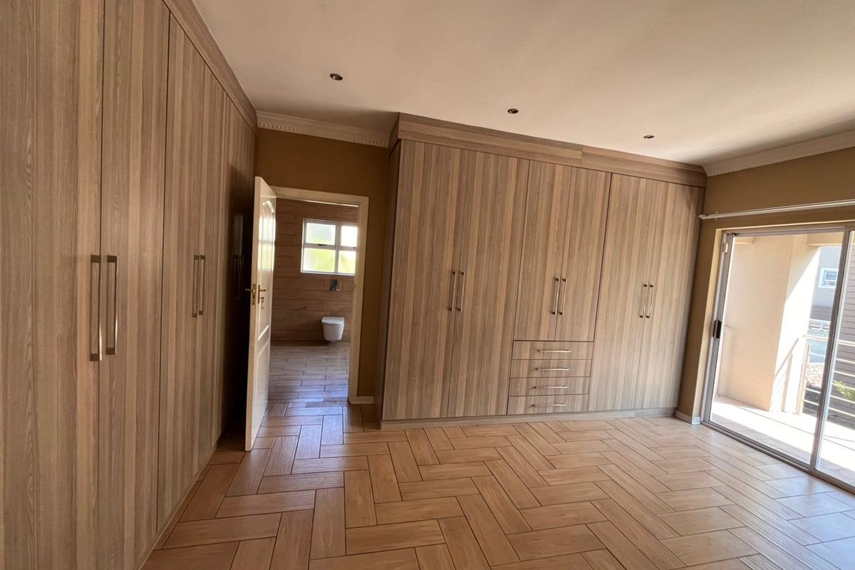 Spacious bedroom featuring extensive built-in wooden cabinetry, herringbone-patterned tiled flooring, recessed ceiling lighting, and direct access to an outdoor balcony.