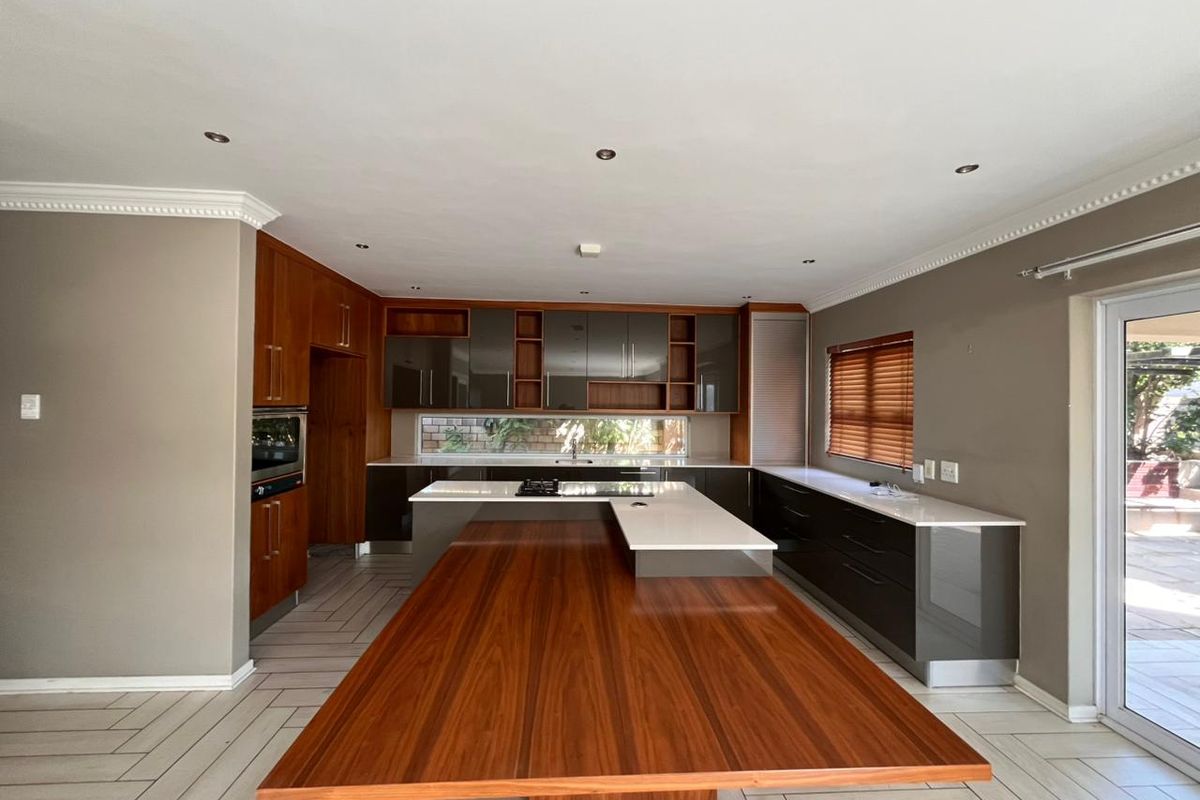 Modern kitchen featuring a large wooden breakfast bar, integrated cabinetry, stone countertops, and a built-in oven, with direct access to the outdoor patio area.